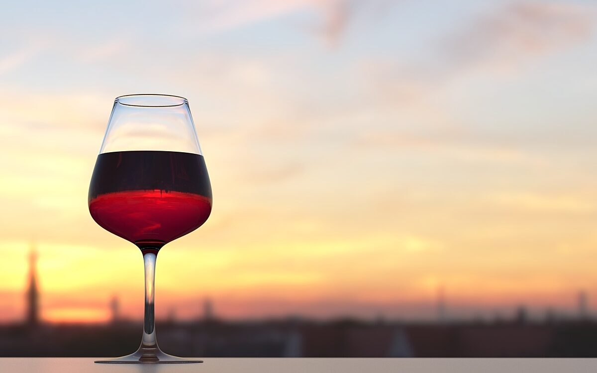 Weinglas mit Rotwein und Sonnenuntergang im Hintergrund Weinglas mit Rotwein und Sonnenuntergang im Hintergrund